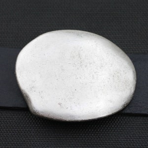 May include: A silver-toned metal buckle with a rounded, slightly irregular shape. The buckle is smooth and has a slightly textured surface.