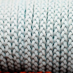 May include: Close-up of a light blue braided leather cord. The cord is made of multiple strands of leather that are woven together to create a braided pattern.