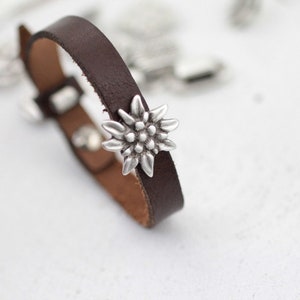 May include: A brown leather bracelet with a silver edelweiss charm.