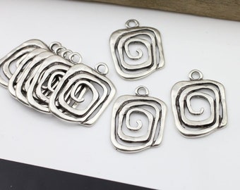 Op de afbeelding: Zilverkleurige metalen bedels met een vierkante vorm en een spiraalvormig ontwerp. De bedels hebben een gat aan de bovenkant om aan sieraden te bevestigen.