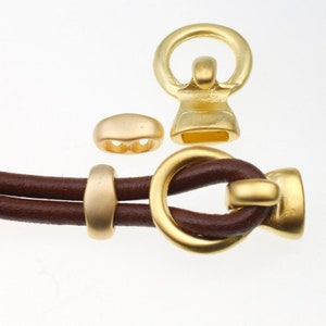 Può includere: Chiusure e perline in metallo dorato per braccialetti in cordoncino di cuoio. Le chiusure hanno un anello e una forma a barilotto. Le perline sono rotonde e hanno una finitura liscia.