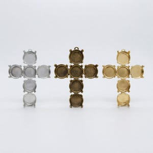 May include: Three cross-shaped pendant settings arranged in a row. Each setting features five circular bezel cups with prongs, designed for holding stones. The left setting is silver-toned, the center is antique bronze, and the right is gold-toned.