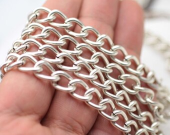 Op de afbeelding: Een zilverkleurige metalen ketting met een reeks in elkaar grijpende ovale schakels. De ketting bestaat uit meerdere strengen van uniforme, gepolijste schakels die een doorlopende, flexibele structuur vormen met een heldere, reflecterende afwerking.