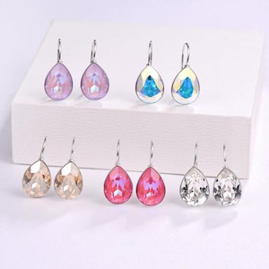 Puede incluir: Surtido de pendientes colgantes con cristales en forma de lágrima en varios colores, incluyendo transparente, rosa y azul. Los pendientes son plateados y tienen un diseño sencillo.