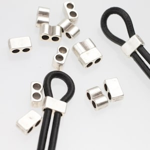 May include: Silver-toned metal cord ends with two holes for threading leather cord. The cord ends are shown with black leather cord threaded through them.