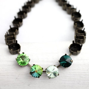 May include: A necklace featuring a series of dark metal settings connected by small links. The necklace has a series of green and clear faceted gemstones. The gemstones are round and vary in shades of green.