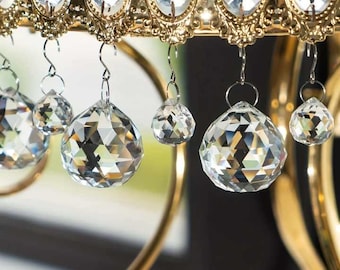 May include: A close-up of a gold-toned metal chandelier with clear crystal prism drops hanging from it. The chandelier has a decorative design with a series of small, round, clear crystals.