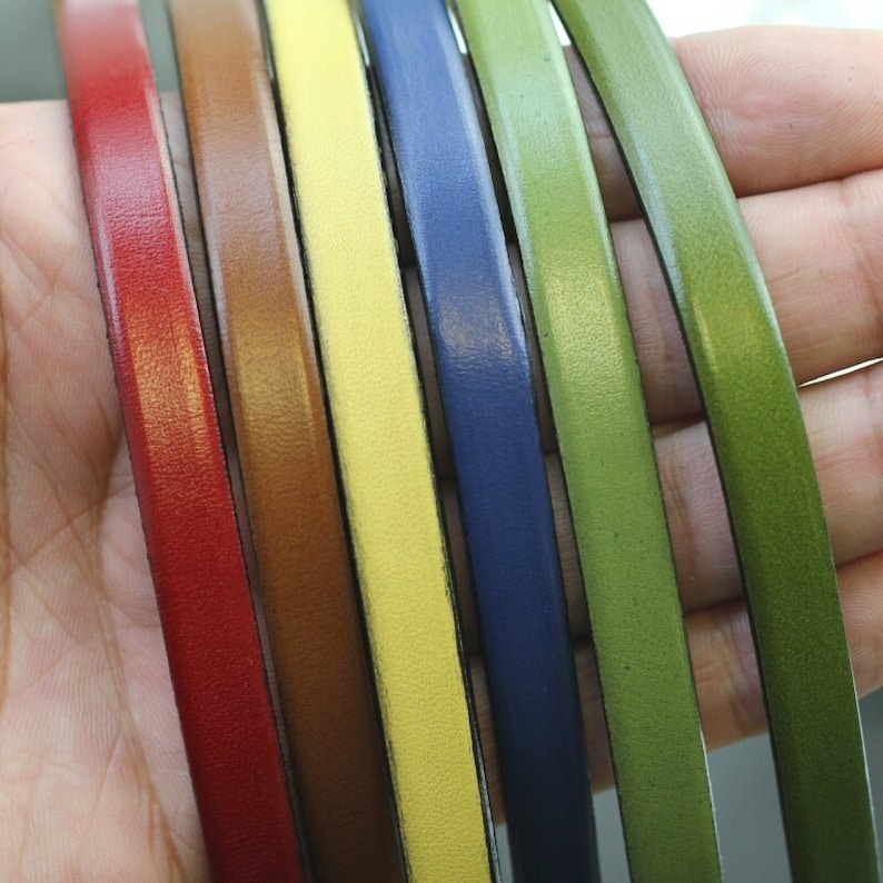 May include: Six leather cords in different colors: red, brown, yellow, blue, green, and dark green. The cords are arranged in a row, with the red cord on the left and the dark green cord on the right.