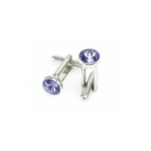 May include: A pair of silver cufflinks with round, light purple gemstones. The cufflinks have a classic design with a post and toggle closure. The gemstones are set in a bezel setting, and the metal has a polished finish.