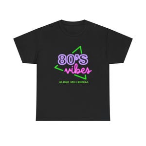 Puede incluir: Camiseta negra con un gráfico de estilo neón que dice "80's vibes" en morado y rosa, con un triángulo verde. Debajo del gráfico, el texto "Elder Millennial" está en verde.