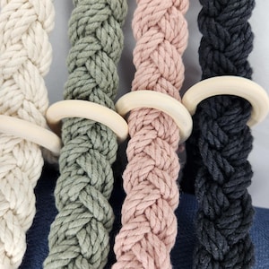 May include: Four braided cotton ropes with wooden rings. The ropes are in natural, green, pink, and black colors.