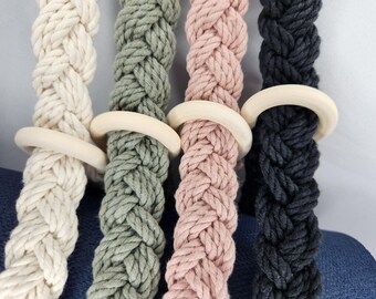 May include: Four braided cotton ropes with wooden rings. The ropes are in natural, green, pink, and black colors.