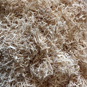 May include: A close-up of a pile of light brown wood shavings. The shavings are very fine and fluffy, and they look like they would be soft to the touch.