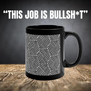 May include: Black ceramic mug with a white geometric pattern and the text "THIS JOB IS BULLSH*T" in white. The mug has a curved handle and is set against a blurred background.