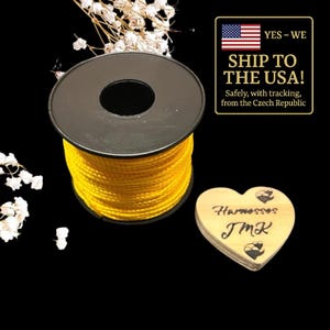 May include: A spool of bright yellow cord with a black center, next to a heart-shaped wooden tag. The tag has the word "Harnesses" and the initials "JMK" engraved on it. The image also includes text that says "Ship to the USA!"