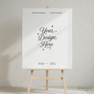 Könnte beinhalten: Ein weißes Leinwand-Mockup auf einer hölzernen Staffelei mit dem Text "Your Design Here" in eleganter Schrift. Oben auf der Leinwand steht "Photoshop + Photopea", unten steht "PSD + JPG". Der Hintergrund ist ein neutrales Off-White.