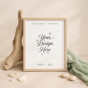 Könnte beinhalten: Gerahmter Mockup mit dem Text "Your Design Here" in eleganter Schrift. Der Rahmen ist aus hellem Holz, und der Hintergrund umfasst ein Stück Treibholz, Muscheln und einen drapierten grünen Stoff. Der Text "Photoshop + Photopea" und "PSD + JPG" sind ebenfalls sichtbar.