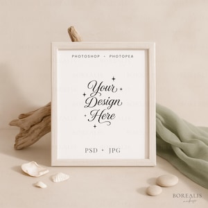 May include: A rectangular, light-colored wooden picture frame with the text "Your Design Here" in elegant script. The frame is surrounded by decorative elements, including seashells, stones, and a green fabric. The words "PHOTOSHOP + PHOTOPEA" and "PSD + JPG" are also visible.