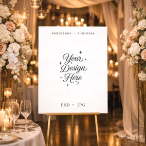 Könnte beinhalten: Ein weißes Schild auf einer goldenen Staffelei mit dem Text "Your Design Here" in eleganter Schrift. Das Schild ist von Blumenarrangements und Kerzen umgeben, was eine warme, einladende Atmosphäre schafft. Die Wörter "Photoshop + Photopea" und "PSD + JPG" sind ebenfalls sichtbar.