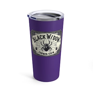 Op de afbeelding: Een paarse reismok met een zilveren deksel. De mok heeft een label met de woorden "Black Widow Cobweb Stew" en een spinnenwebontwerp met een spin in het midden. Het ontwerp is in zwart en wit.