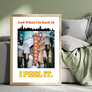 May include: A framed print with a white background and a cityscape silhouette at the top. The text "And When I'm Back In" is in orange letters. A photo of a red "Chicago" sign with streetlights in the foreground is in the center. The text "I FEEL IT." is in yellow letters at the bottom.