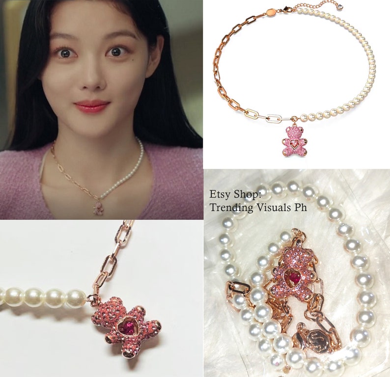 May include: A delicate gold chain necklace with a pink crystal bear charm and a pearl strand. The necklace is layered with a second strand of pearls.