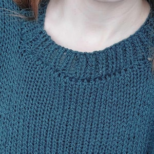 May include: A teal blue knitted jumper with a ribbed texture and a round neckline.