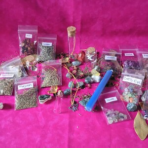 May include: An assortment of small glass bottles, clear plastic bags, and crystals are arranged on a bright pink surface. The bags contain dried herbs and crystals, labeled with names like "Rose," "Lavender," and "Cats Eye." A blue candle and a butterfly pendant are also present.