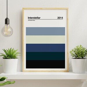 Può includere: Stampa artistica incorniciata con una tavolozza di colori ispirata al film "Interstellar". Il design include bande orizzontali di blu, grigio e nero, con il titolo del film e l'anno 2014 in alto. L'opera d'arte è esposta su una mensola bianca con piante in vaso.