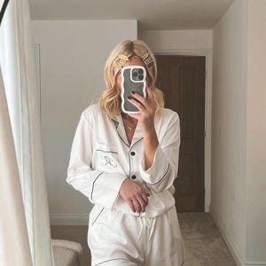 May include: White satin pajama set with black trim and a black embroidered initial. The set includes a long-sleeved shirt and shorts.