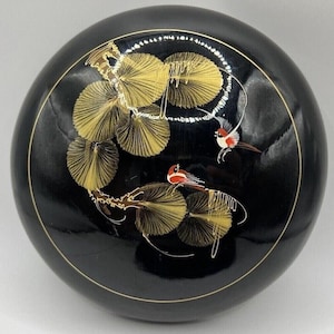 May include: A round, black decorative box with a gold rim and detailed artwork. The design features gold-coloured fan-shaped leaves and two small birds with red and white markings, creating an elegant, nature-inspired aesthetic.