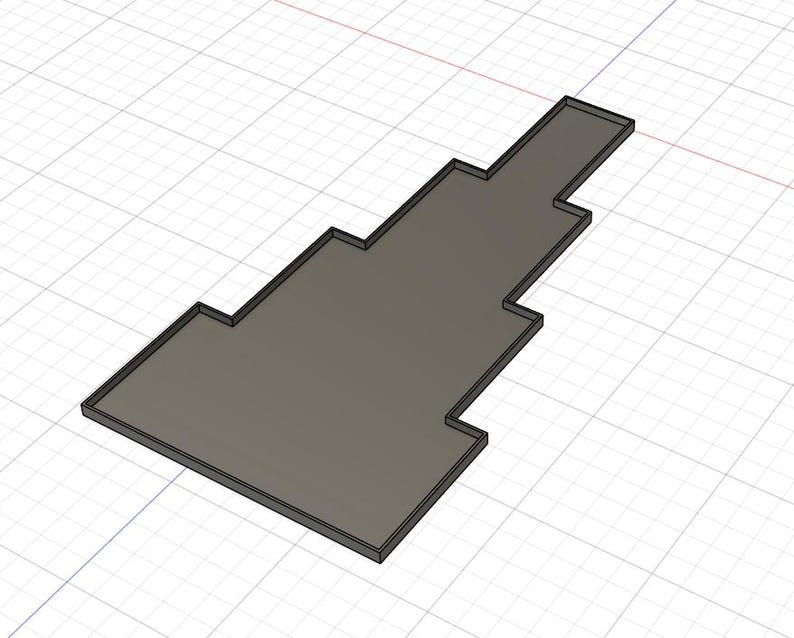 Puede incluir: Objeto rectangular gris renderizado en 3D con un dise&ntilde;o escalonado. El objeto tiene un borde gris oscuro y se encuentra sobre un fondo de cuadr&iacute;cula. La forma recuerda a una alfombra de suelo o una pieza cortada a medida.
