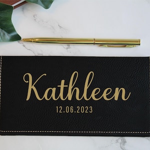 May include: Black leather checkbook cover with gold stitching and the name "Kathleen" and the date "12.06.2023" embossed in gold.