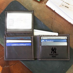 May include: Open brown leather wallet with multiple card slots and a clear ID window. The wallet is filled with cards and cash. The text "YOUR TEXT HERE" is below a black NY logo.