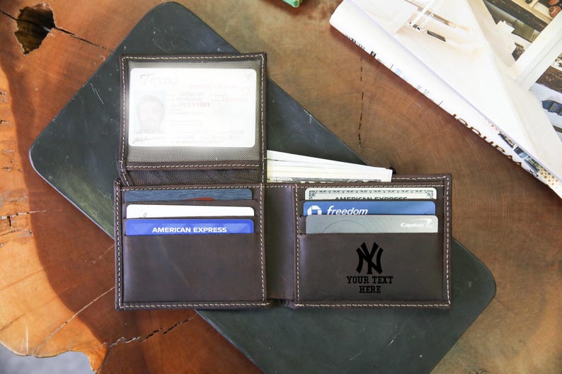 May include: Open brown leather wallet with multiple card slots and a clear ID window. The wallet is filled with cards and cash. The text "YOUR TEXT HERE" is below a black NY logo.