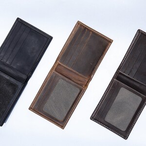 May include: Three leather wallets in different colors: black, brown, and dark gray. Each wallet has a flap closure and a clear plastic window for an ID card.