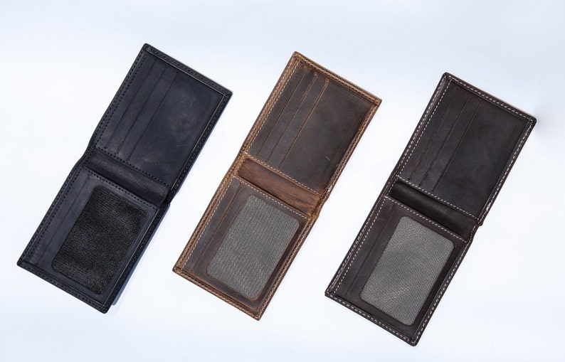May include: Three leather wallets in different colors: black, brown, and dark gray. Each wallet has a flap closure and a clear plastic window for an ID card.