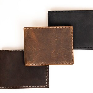 May include: Three leather wallets in different shades of brown. The top wallet is a light brown, the middle wallet is a medium brown, and the bottom wallet is a dark brown.
