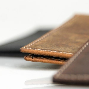 May include: Close-up of two leather wallets with white stitching. The top wallet is brown and the bottom wallet is dark brown.