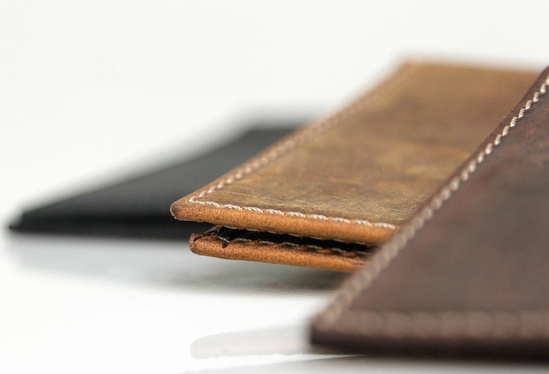 May include: Close-up of two leather wallets with white stitching. The top wallet is brown and the bottom wallet is dark brown.