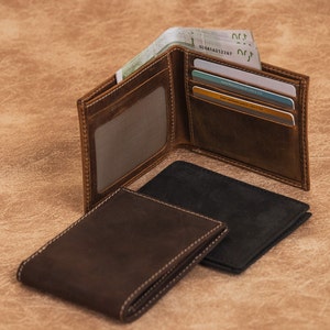 May include: Three leather wallets, two brown and one black, with one open to reveal cash and credit cards. The open wallet has a clear plastic window for an ID card.