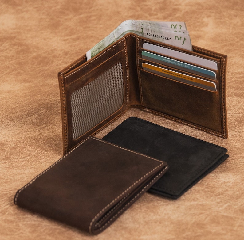 May include: Three leather wallets, two brown and one black, with one open to reveal cash and credit cards. The open wallet has a clear plastic window for an ID card.