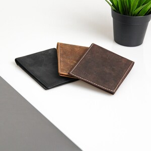 May include: Three leather wallets in black, brown, and dark brown. The wallets are laid out on a white surface.