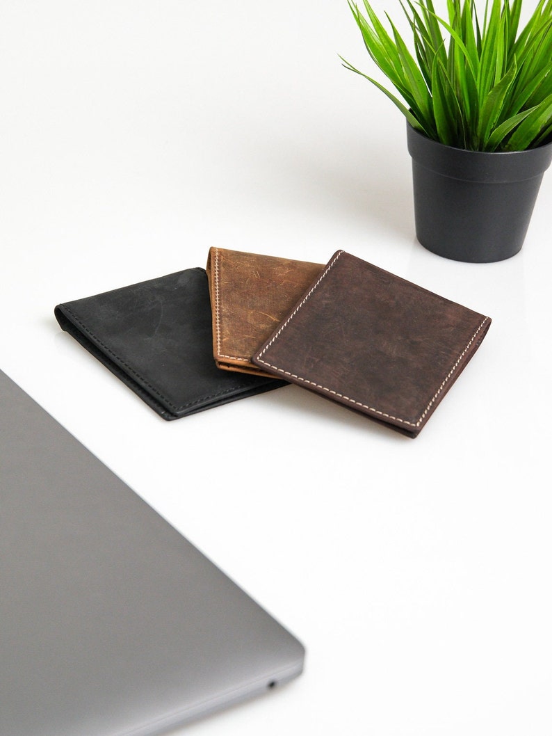 May include: Three leather wallets in black, brown, and dark brown. The wallets are laid out on a white surface.