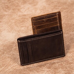 Pu&ograve; includere: Due portafogli in pelle, uno marrone e uno nero, con cuciture bianche. Entrambi i portafogli hanno pi&ugrave; slot per carte.