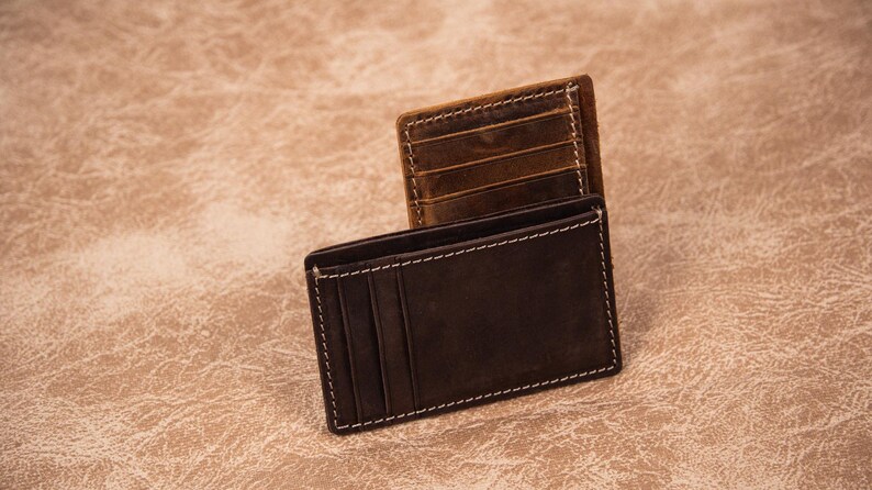 Pu&ograve; includere: Due portafogli in pelle, uno marrone e uno nero, con cuciture bianche. Entrambi i portafogli hanno pi&ugrave; slot per carte.