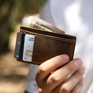 Pu&ograve; includere: Un portafoglio in pelle marrone con una carta di credito e contanti all'interno. Il portafoglio &egrave; aperto e la carta di credito &egrave; visibile. I contanti sono piegati e riposti nel portafoglio.