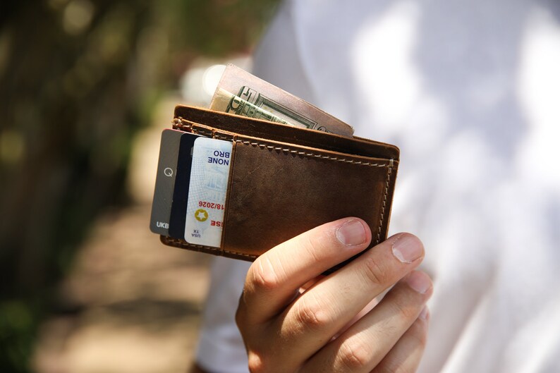 Pu&ograve; includere: Un portafoglio in pelle marrone con una carta di credito e contanti all'interno. Il portafoglio &egrave; aperto e la carta di credito &egrave; visibile. I contanti sono piegati e riposti nel portafoglio.