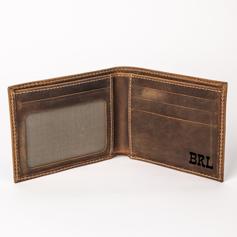 May include: A brown leather wallet with a stitched edge and a window for an ID card. The wallet has a personalized inscription that reads "BRL".