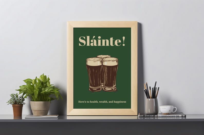 May include: A framed print with a green background and the text "Sl&aacute;inte!" in a white font. Three glasses of dark beer are depicted below the text. The text "Here's to health, wealth, and happiness" is at the bottom of the print.